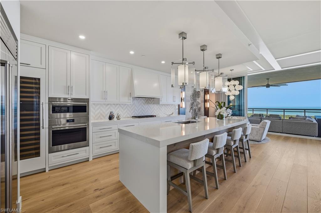 13945 Old Coast Road, Unit PH05 Naples, FL 34110 - Photo 8 of 37 a kitchen with kitchen island granite countertop a table chairs microwave and cabinets