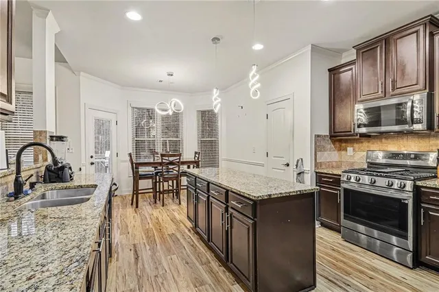 a kitchen with stainless steel appliances granite countertop a stove top oven a sink dishwasher a dining table and chairs with wooden floor