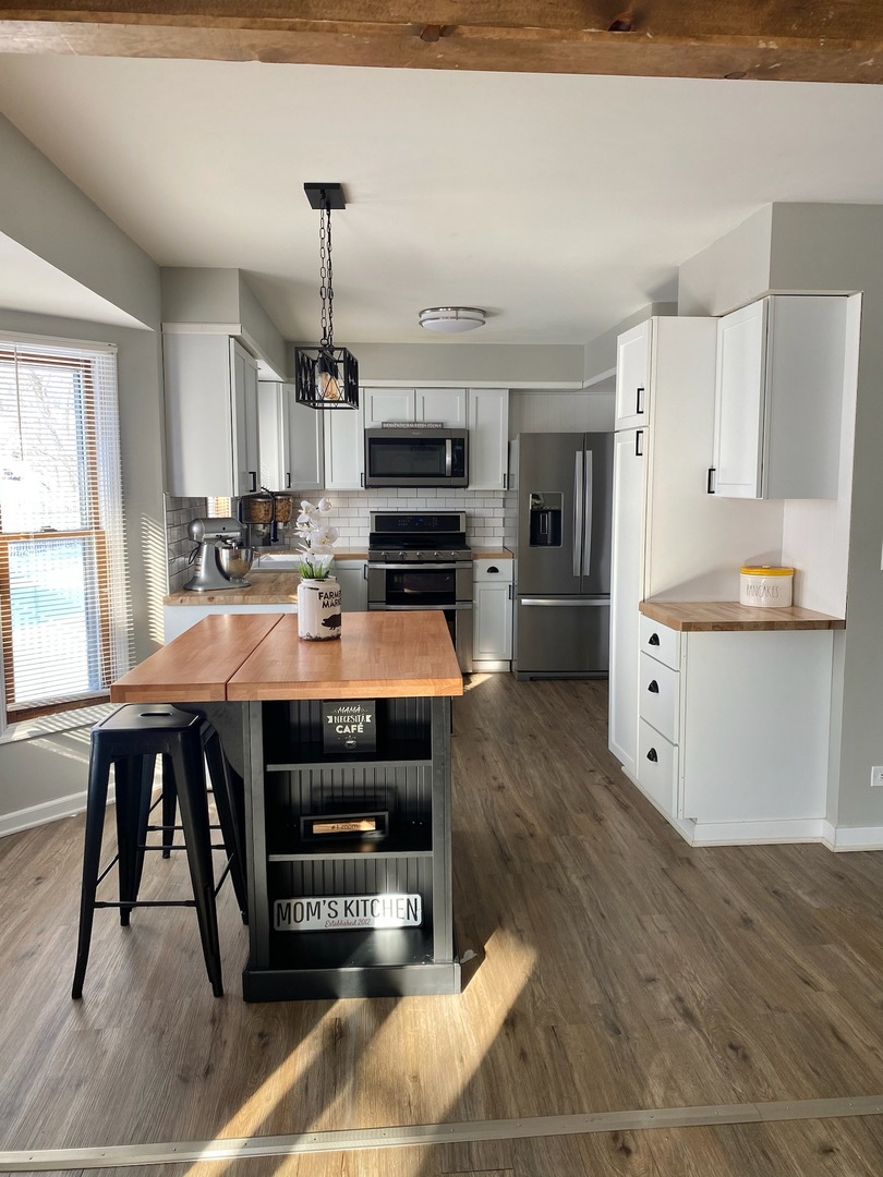 90 Decker Drive Cary, IL 60013 - Photo 2 of 12 a kitchen with kitchen island a stove a refrigerator and a dining table with wooden floor