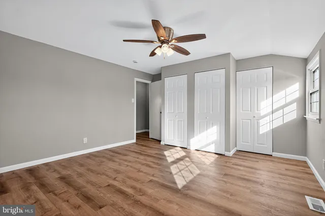 a view of an empty room with wooden floor and a ceiling fan