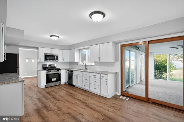 a kitchen with stainless steel appliances granite countertop a stove top oven a sink dishwasher a refrigerator and white cabinets with wooden floor