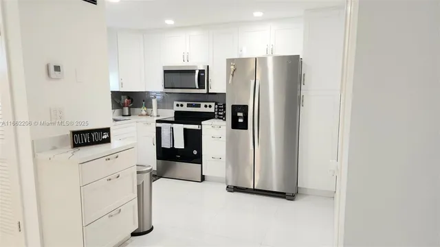 a kitchen with stainless steel appliances a refrigerator a sink and white cabinets