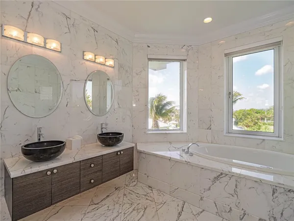a bathroom with a double vanity sink a mirror and a bathtub next to a window