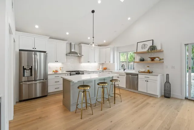 a kitchen with stainless steel appliances granite countertop a refrigerator a sink dishwasher a stove and white cabinets with wooden floor