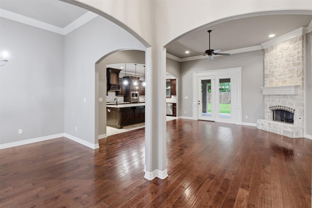 7765 Hickory Spring Lane Tyler, TX 75703 - Photo 6 of 38 Spacious room featuring rich wood-finish flooring, a stone-clad fireplace with a hearth, double French doors leading to exterior space, and an arched entryway