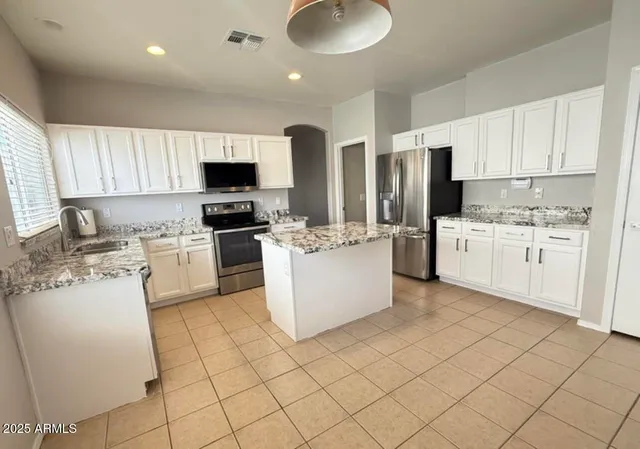 a kitchen with stainless steel appliances granite countertop a stove top oven a sink a refrigerator and white cabinets
