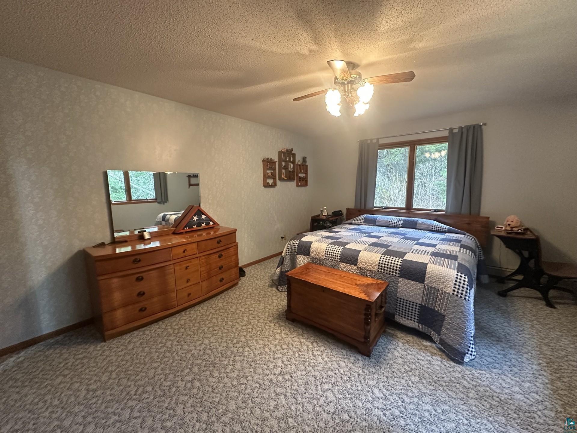 81 Hautaluoma Road Esko, MN 55733 - Photo 17 of 43 Spacious bedroom featuring patterned wall coverings, a ceiling fan with integrated lighting, and a large window providing natural illumination