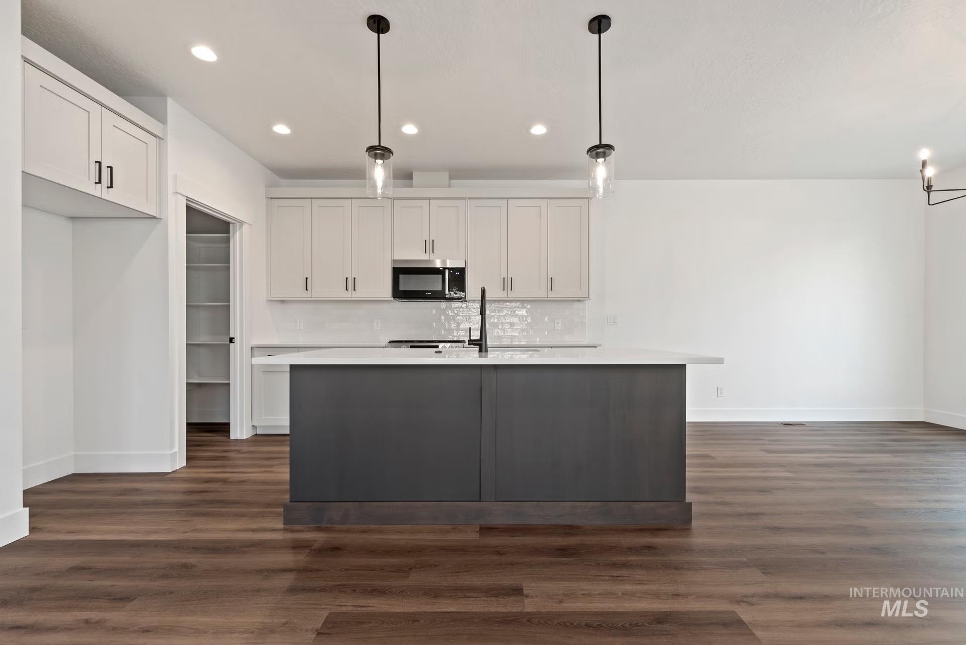 748 South Calhoun Place Star, ID 83669 - Photo 13 of 32 Kitchen with dark wood finished floors, decorative light fixtures, a kitchen island with sink, tasteful backsplash, and dual tone cabinets