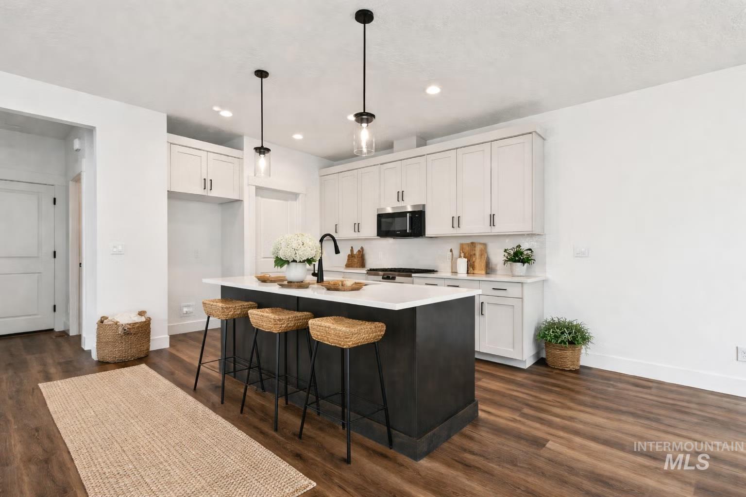 748 South Calhoun Place Star, ID 83669 - Photo 2 of 32 Dual tone kitchen with decorative light fixtures, a breakfast bar area, dark wood-style flooring, a kitchen island with sink, and stainless steel appliances
