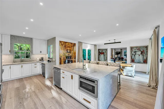 a large white kitchen with a stove a sink dishwasher and a dining table with wooden floor