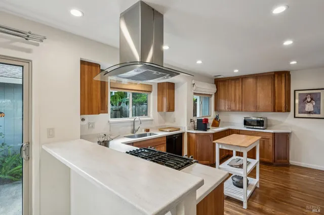 a kitchen with a stove a sink a kitchen island with chairs and wooden cabinets