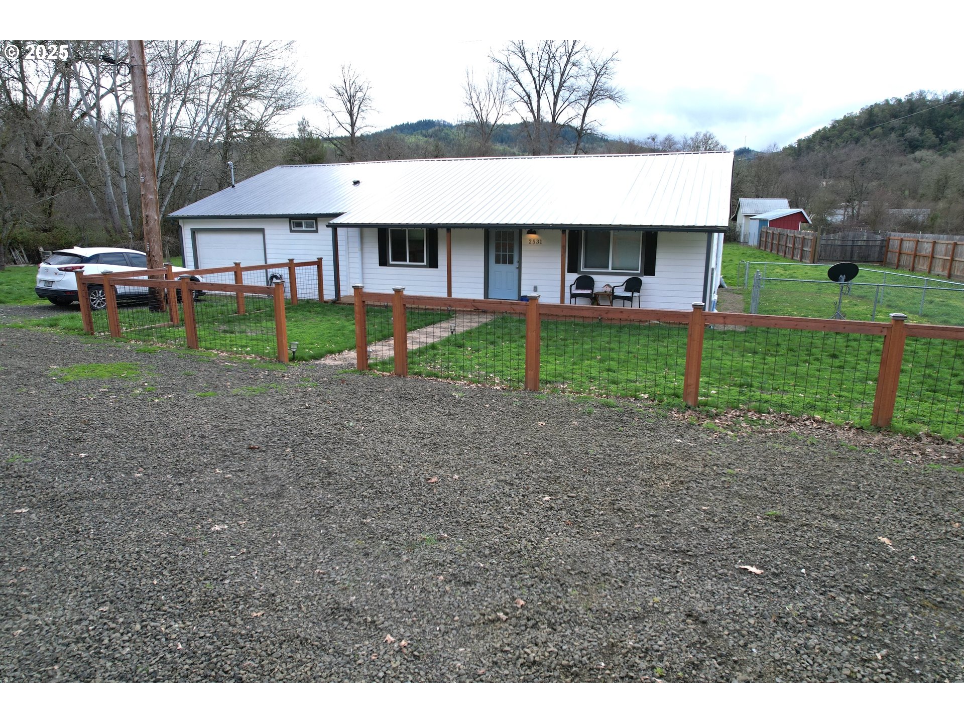 a view of house in front of a big yard with plants and large trees