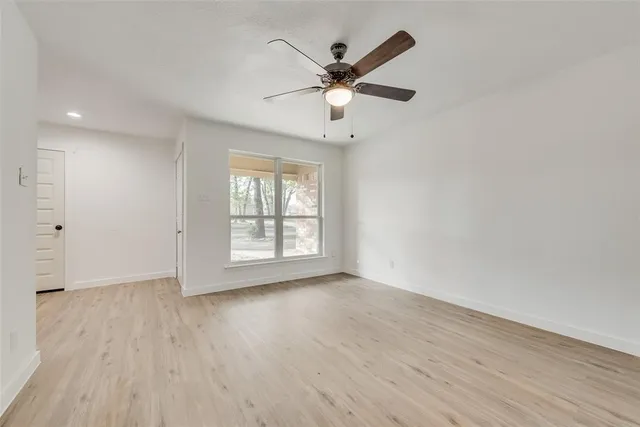 an empty room with wooden floor fan and windows
