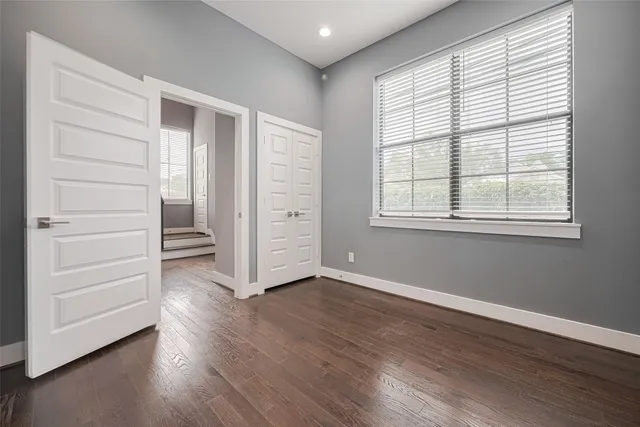 an empty room with wooden floor closet and windows