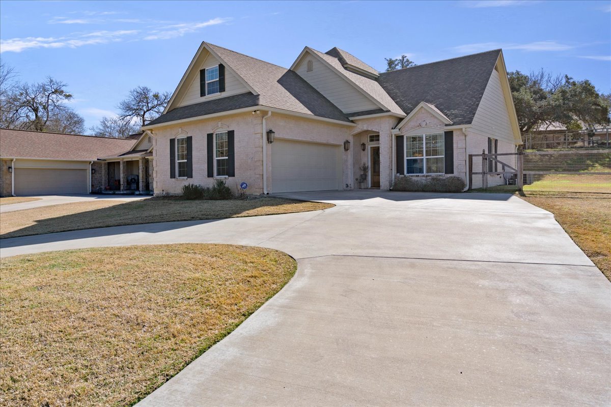View of front of property featuring curved driveway, an attached garage, brick siding, and roof with shingles