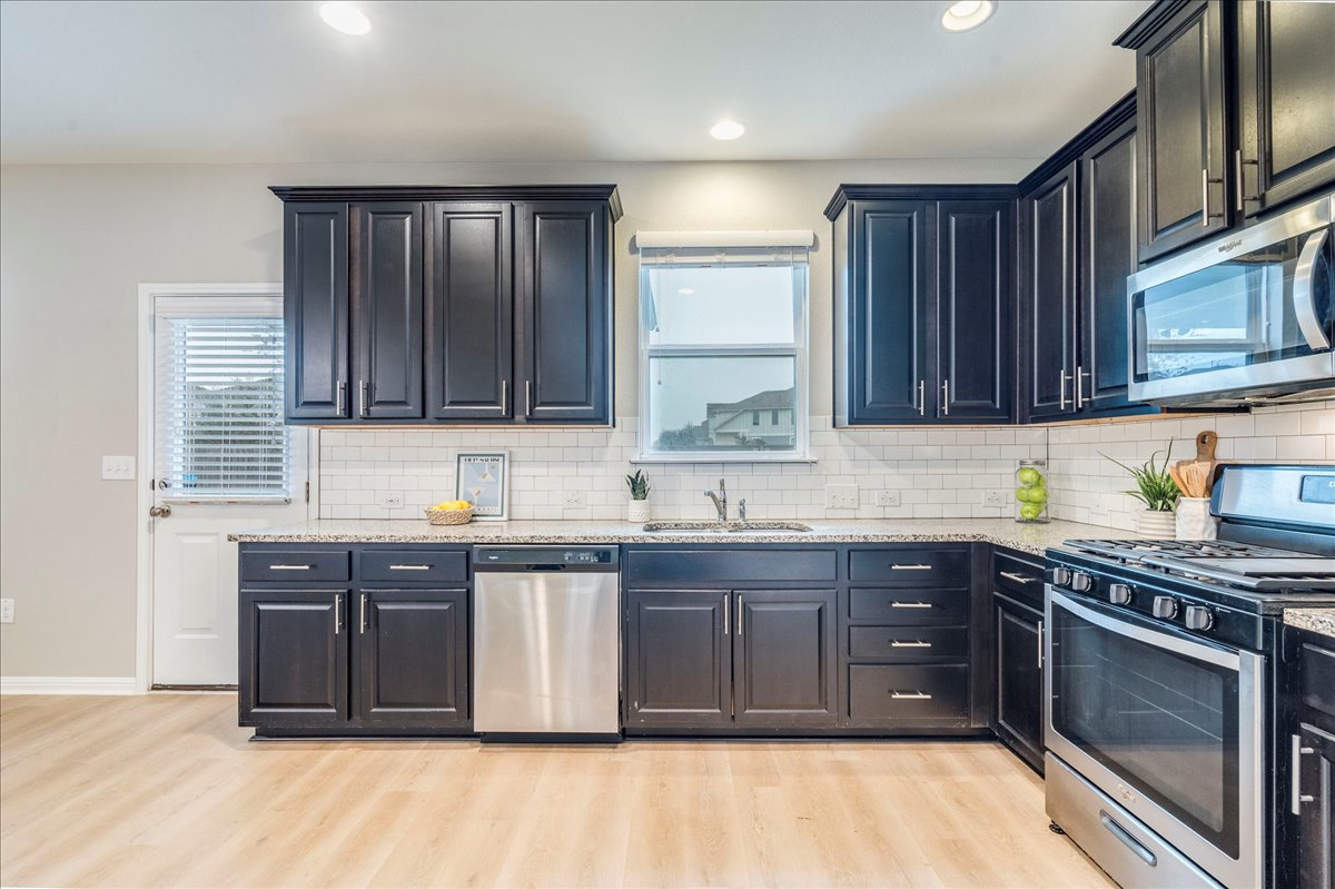 Kitchen with appliances with stainless steel finishes, light stone countertops, backsplash, light wood-type flooring, and recessed lighting