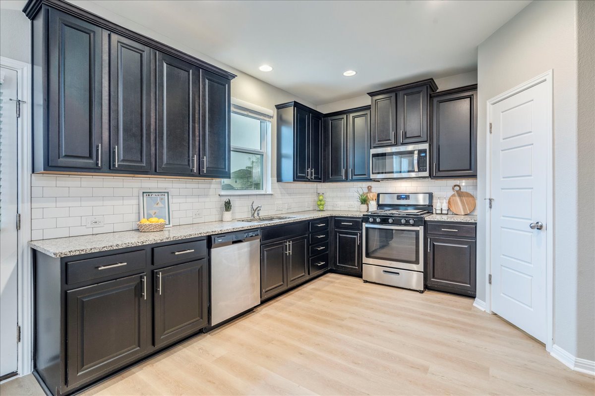 Kitchen featuring appliances with stainless steel finishes, light stone counters, dark cabinets, light wood-style flooring, and recessed lighting