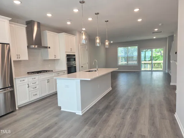 a large kitchen with stainless steel appliances a large counter top a stove a refrigerator cabinets and a wooden floor