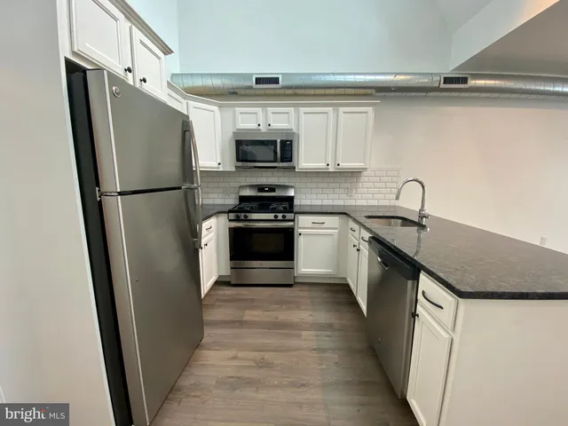 a kitchen with stainless steel appliances a refrigerator a sink a stove top oven and wooden floor