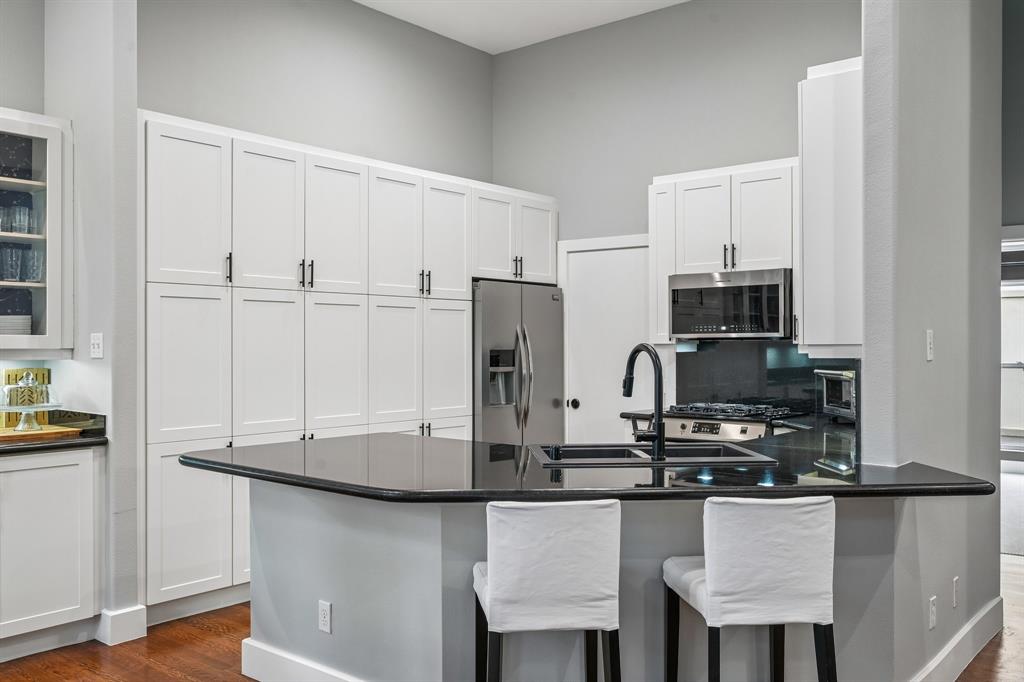 3553 Wheeler Street Dallas, TX 75209 - Photo 13 of 35 Kitchen with white shaker cabinetry, black granite countertops, stainless steel appliances, breakfast bar seating, and abundant pantry storage