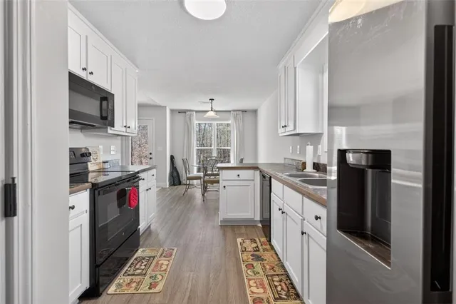 a kitchen with stainless steel appliances granite countertop a refrigerator stove a sink dishwasher and white cabinets with wooden floor