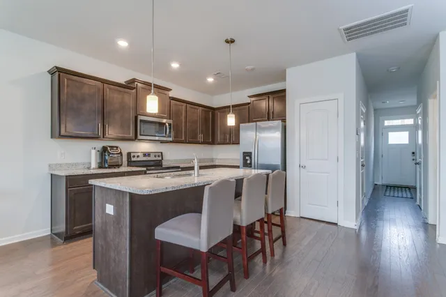 a kitchen with stainless steel appliances granite countertop a stove top oven a sink dishwasher a refrigerator and a dining table with wooden floor
