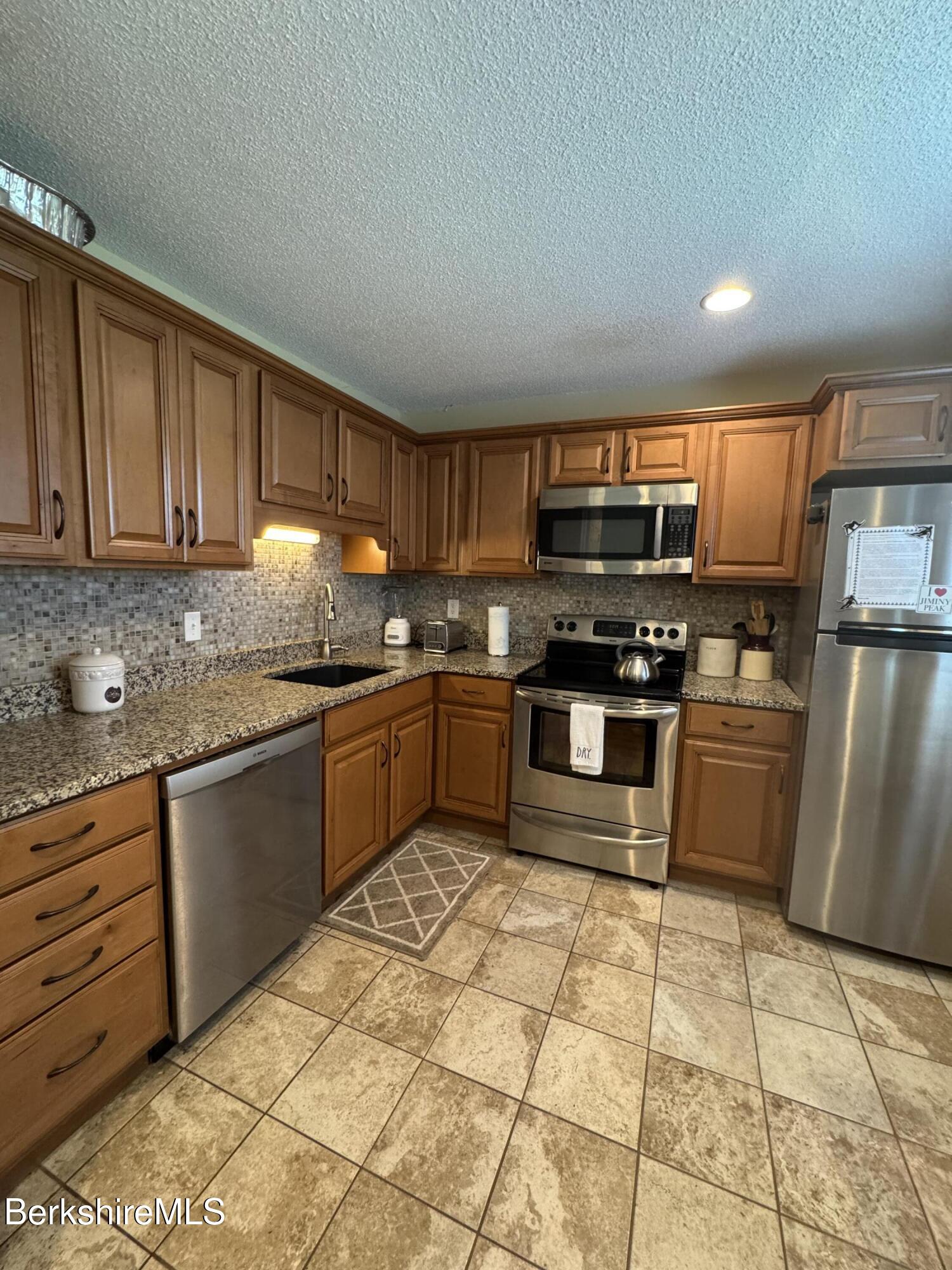 37 Corey Road, Unit 73 Hancock, MA 01237 - Photo 17 of 24 a kitchen with stainless steel appliances granite countertop a stove top oven a sink a counter top space and cabinets