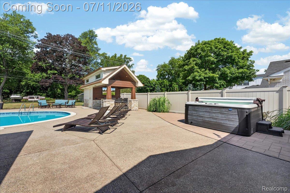 23750 East River Road Grosse Ile, MI 48138 - Photo 39 of 54 Outdoor living space featuring an in-ground swimming pool, a dedicated hot tub area with stone-look pavers, and a pool house with a covered patio