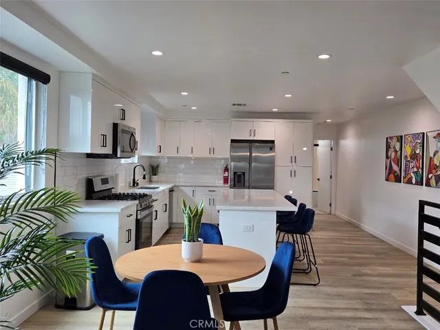 a kitchen with stainless steel appliances a dining table chairs refrigerator and sink