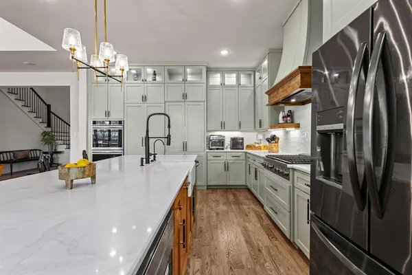 a kitchen with stainless steel appliances a sink a stove top oven a chimney cabinets and wooden floor