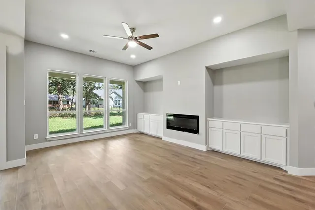 an empty room with wooden floor fan and windows