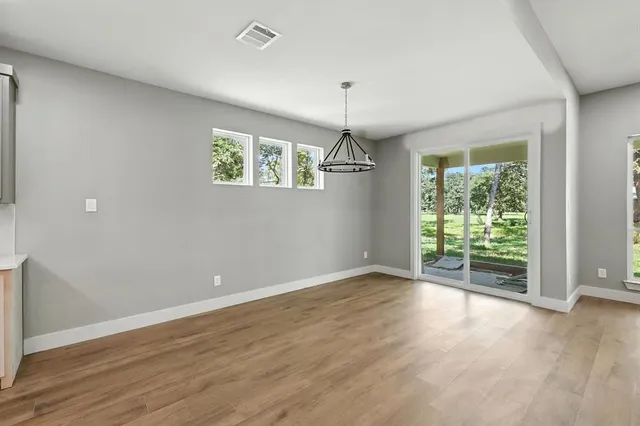 an empty room with wooden floor chandelier and windows
