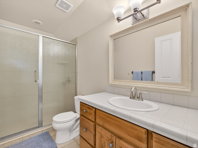 557 Craftsman Way Midway, UT 84049 - Photo 43 of 59 Bathroom featuring a shower with framed frosted glass enclosure, a vanity with wood cabinetry, a tile countertop, and a framed mirror with a three-light fixture