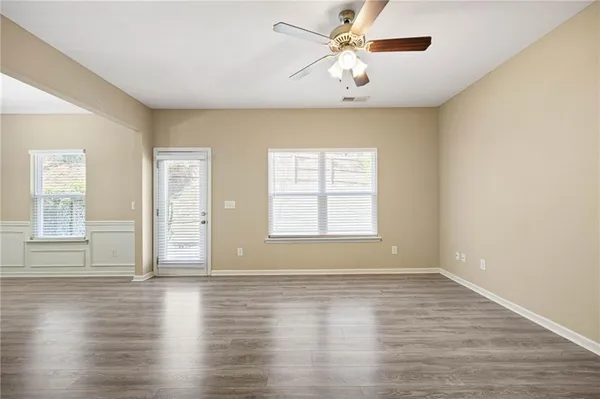 an empty room with wooden floor chandelier fan and windows