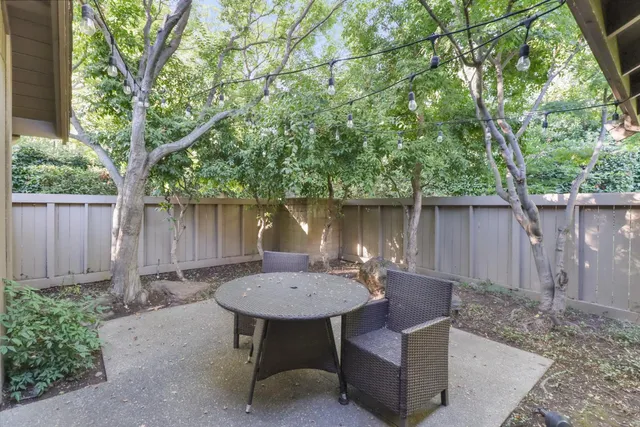 a view of a backyard with table and chairs potted plants and a large tree