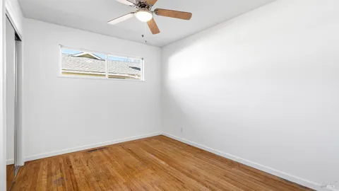 an empty room with wooden floor ceiling fan and windows