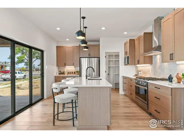 a large kitchen with stainless steel appliances kitchen island granite countertop a stove a refrigerator a sink and white cabinets with wooden floor