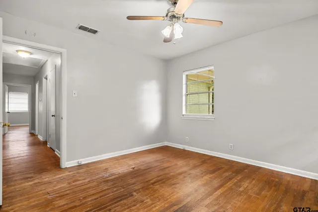 an empty room with wooden floor chandelier fan and windows