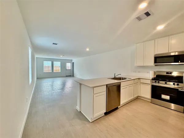 a kitchen with stainless steel appliances granite countertop a stove top oven a sink dishwasher and a refrigerator with wooden floor