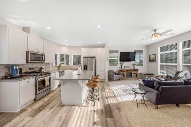 a view of a kitchen with kitchen island stainless steel appliances a stove a sink a refrigerator cabinets and living room view