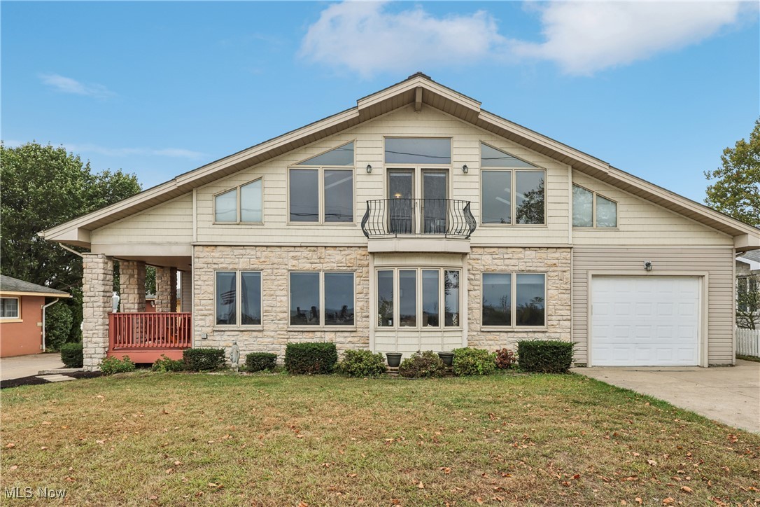View of front of home featuring a balcony, stone siding, a front yard, a garage, and concrete driveway