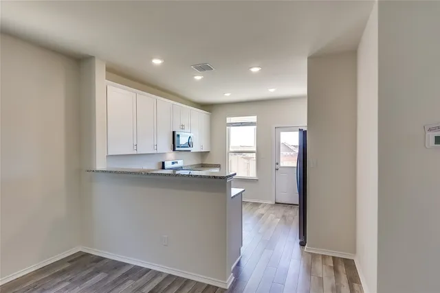 a kitchen with stainless steel appliances granite countertop a refrigerator a sink dishwasher a stove and white countertops with wooden floor