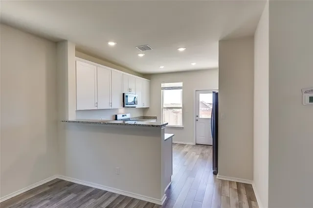 a kitchen with stainless steel appliances granite countertop a refrigerator a sink dishwasher a stove and white countertops with wooden floor