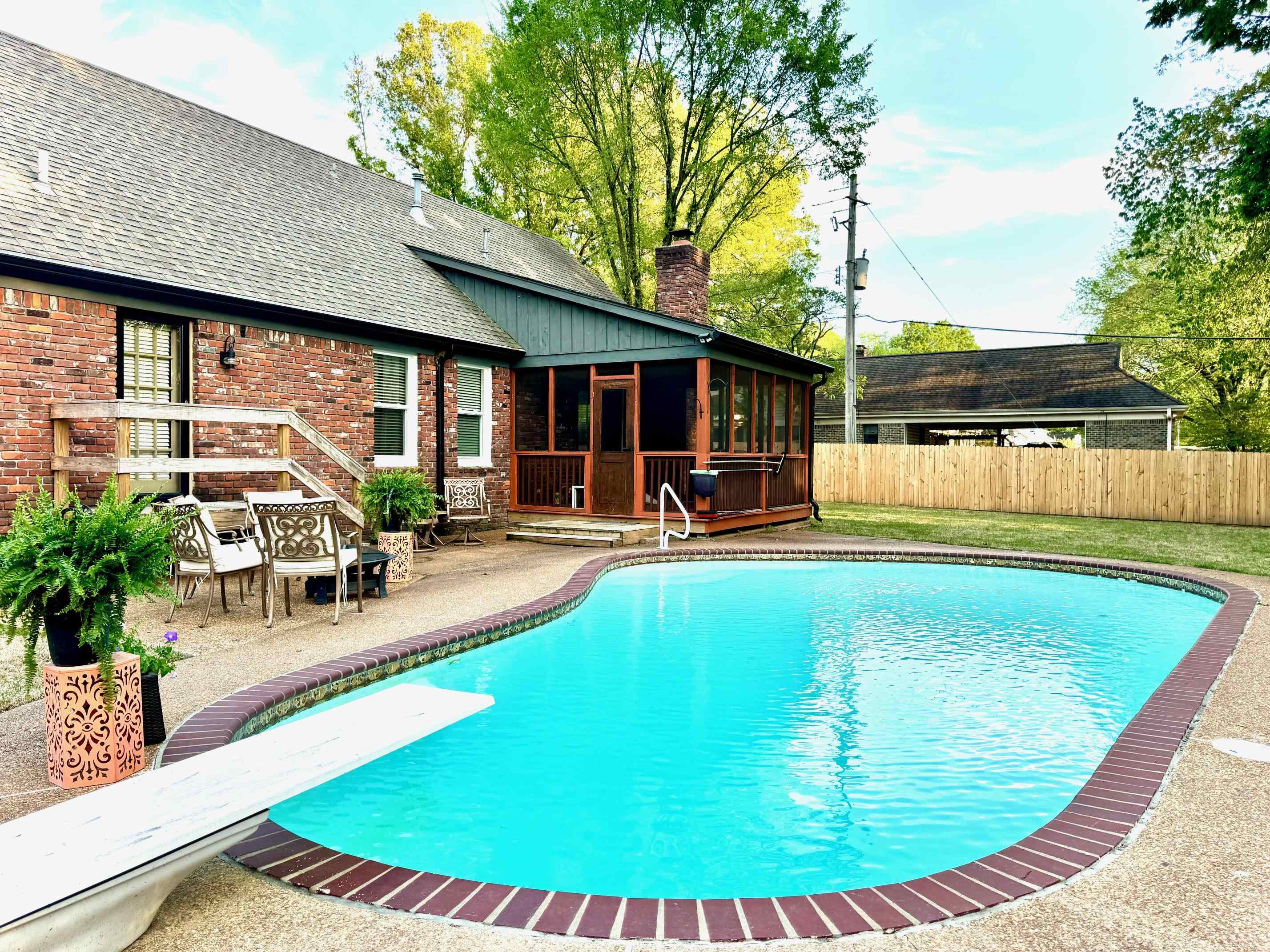 View of swimming pool featuring a sunroom, patio surround, a wooden deck, and a diving board