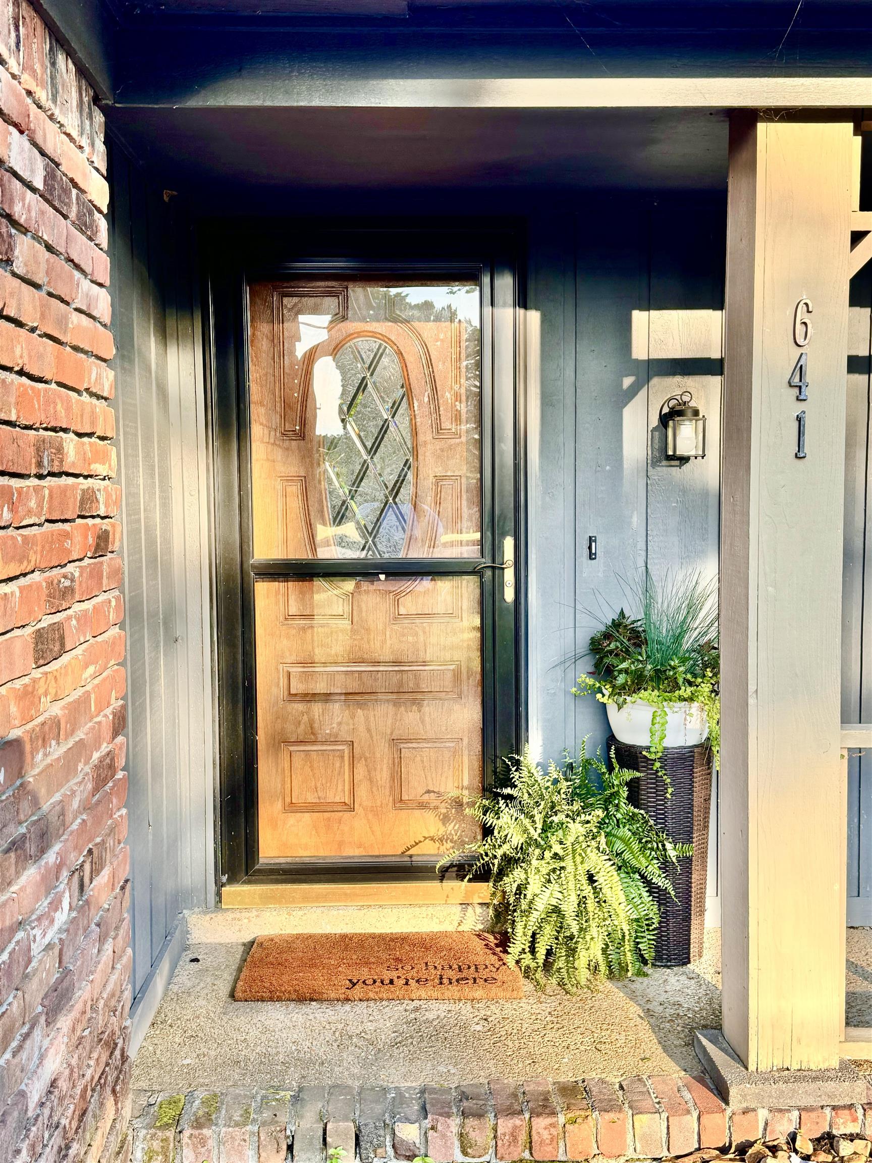 641 Hermitage Trail Collierville, TN 38017 - Photo 2 of 24 Brick facade featuring a natural wood-finish entry door with decorative glass paneling, set against vertical siding and a visible exterior light fixture