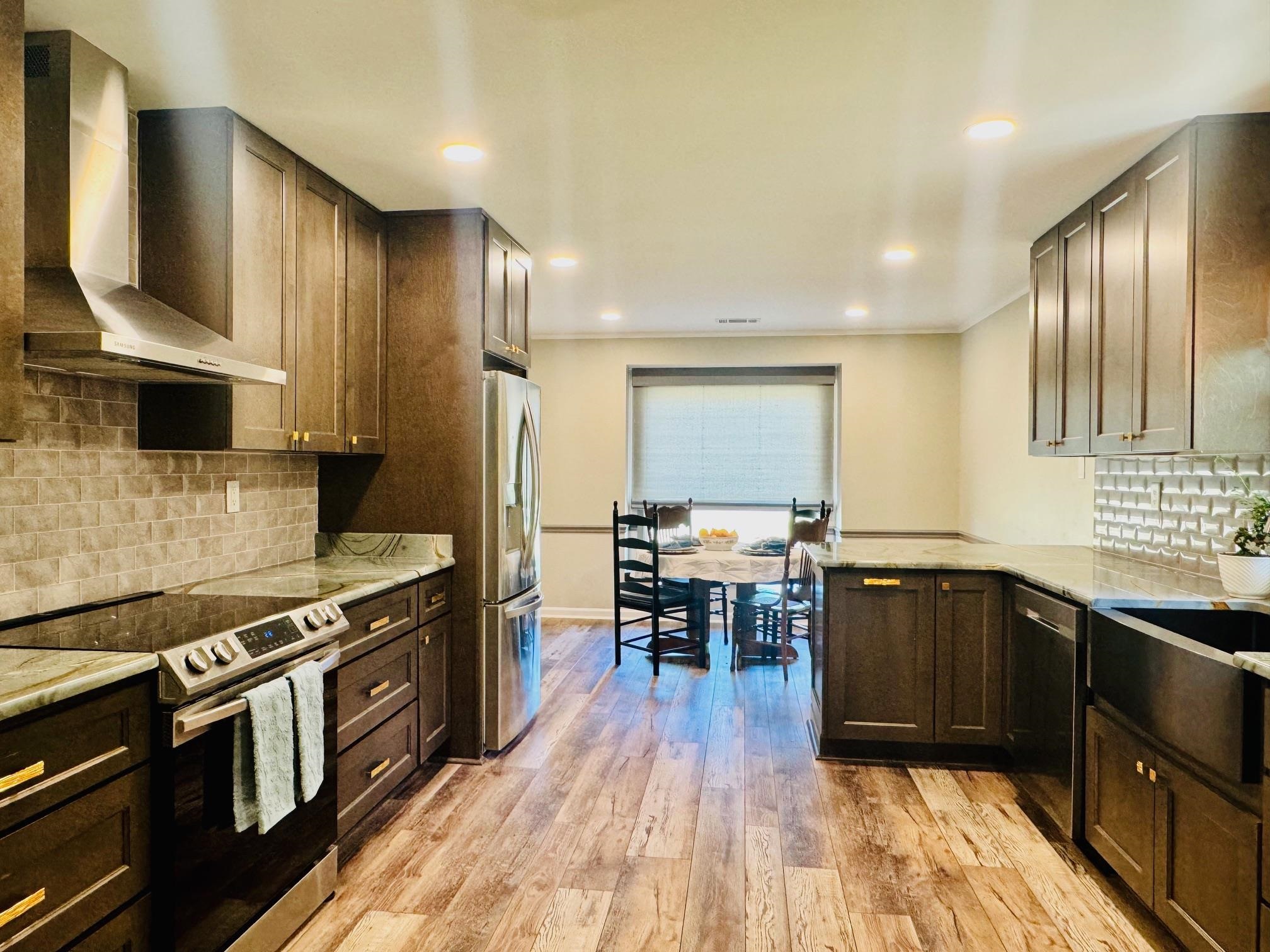 641 Hermitage Trail Collierville, TN 38017 - Photo 6 of 24 Kitchen featuring decorative backsplash, stainless steel appliances, light stone counters, light wood-type flooring, and dark wood finish cabinetry
