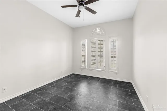 an empty room with chandelier fan and windows