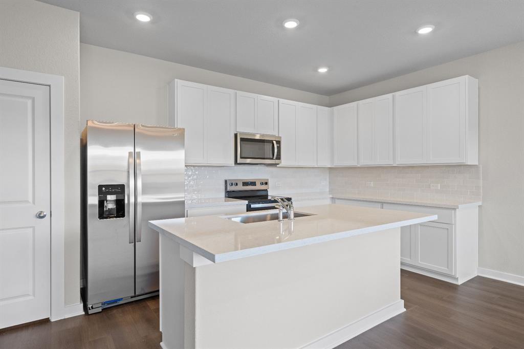 177 Sleep Hollow Jarrell, TX 76537 - Photo 7 of 24 Kitchen featuring an island with an undermount sink, white cabinetry, stainless steel appliances, a white subway tile backsplash, and wood-finish flooring