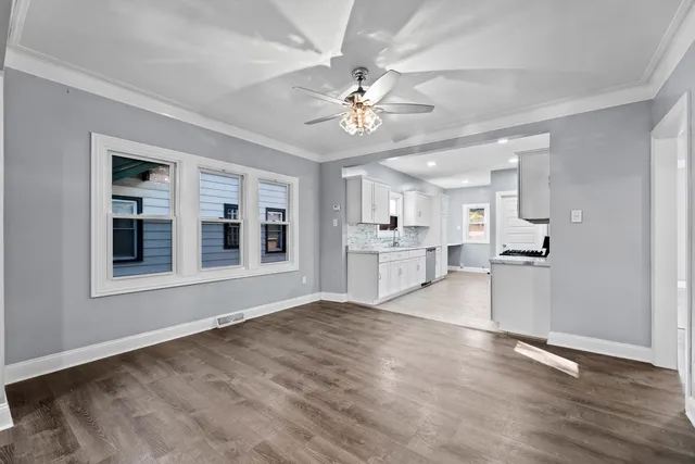 a view of an empty room with kitchen and window
