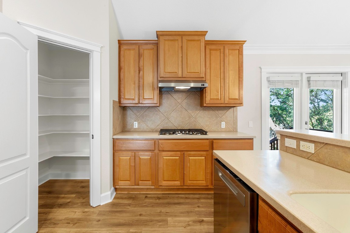 10805 Ariock Lane Austin, TX 78739 - Photo 11 of 40 Kitchen featuring brown cabinetry, stainless steel appliances, backsplash, dark wood-style floors, and ornamental molding